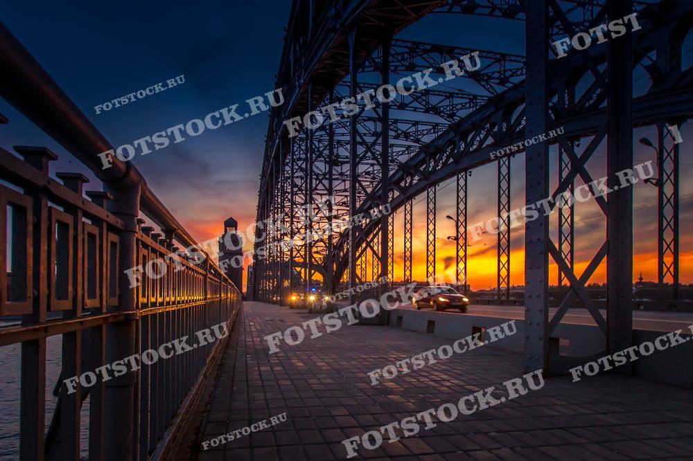 Фотография демонстрирует красочный закат на фоне Большеохтинского моста в Санкт-Петербурге. 
Этот снимок идеально подходит для использования в туристических и художественных публикациях, иллюстрируя уникальную атмосферу города на Неве.